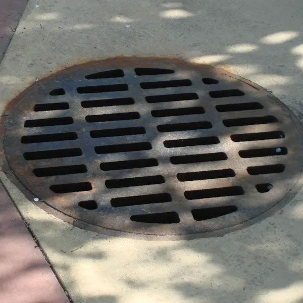 Round storm drain grate embedded in concrete sidewalk